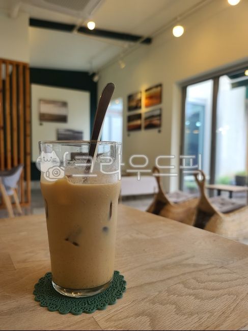 Iced latte,latte,coffee,cafe,cafe interior,indoor space,wooden table,table,glass cup,cup,ice,drink,drink glass,straw,coaster,chair,window,picture frame,wall,indoor lighting,cafe interior,rest area