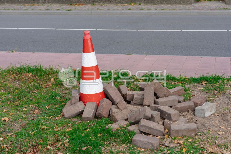 Safety cones,road cones,paving bricks,bricks,construction,maintenance,roadwork,sidewalk,grass,green grass,red,white,gray bricks,pile,traffic safety,cones,outdoor,daytime,street,road,traffic,city,public space