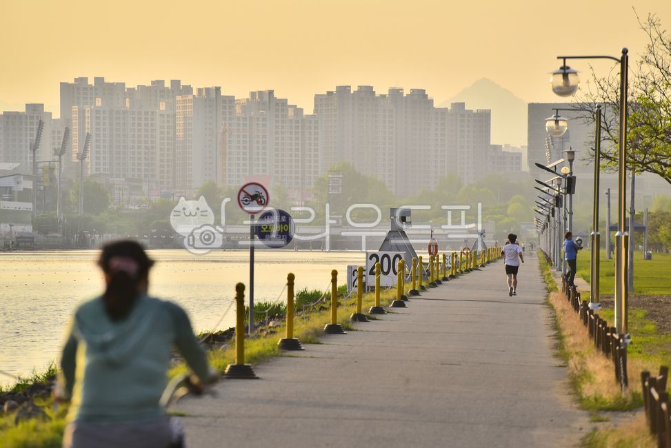 Life sports,information board,bicycle,jogging,road sign,riding,bike,vehicle,Street lamp,running,trail,human,traffic,Apartment village,Dusk,Cardiovascular exercise,transportation,lakeside,outdoors,person,background,sunset,road name,nightfall